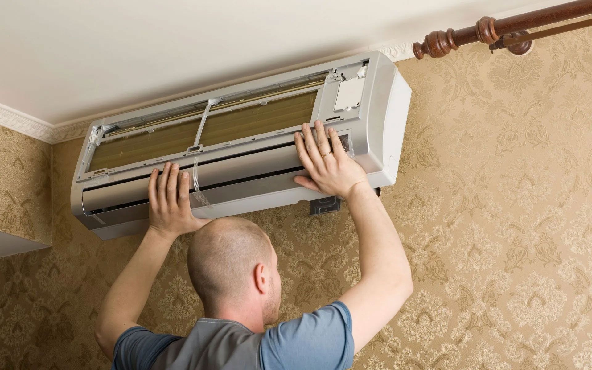 A person installing a silver indoor air conditioning unit onto a patterned wall.
