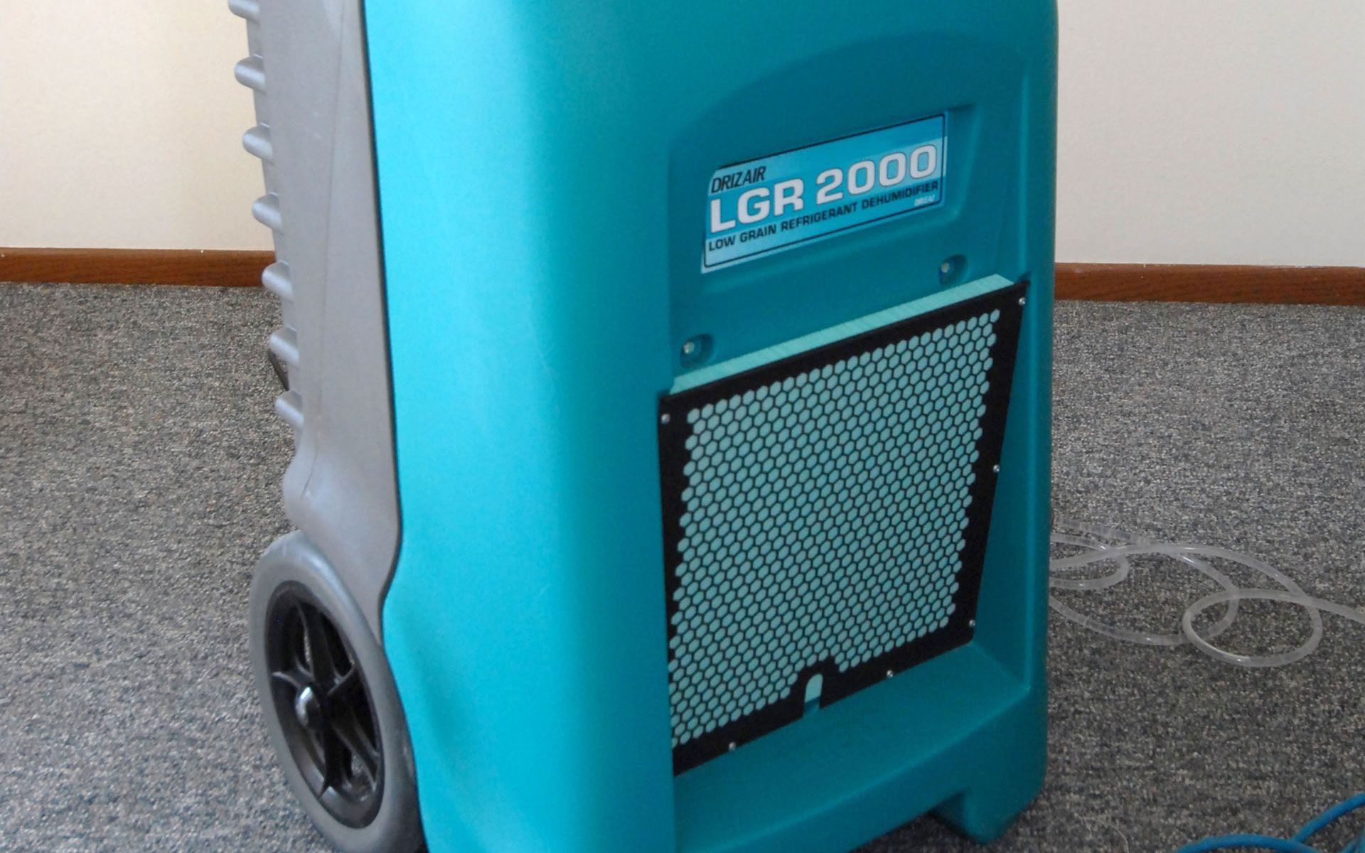 A teal LGR 2000 industrial dehumidifier sits on a carpeted floor against a plain wall.