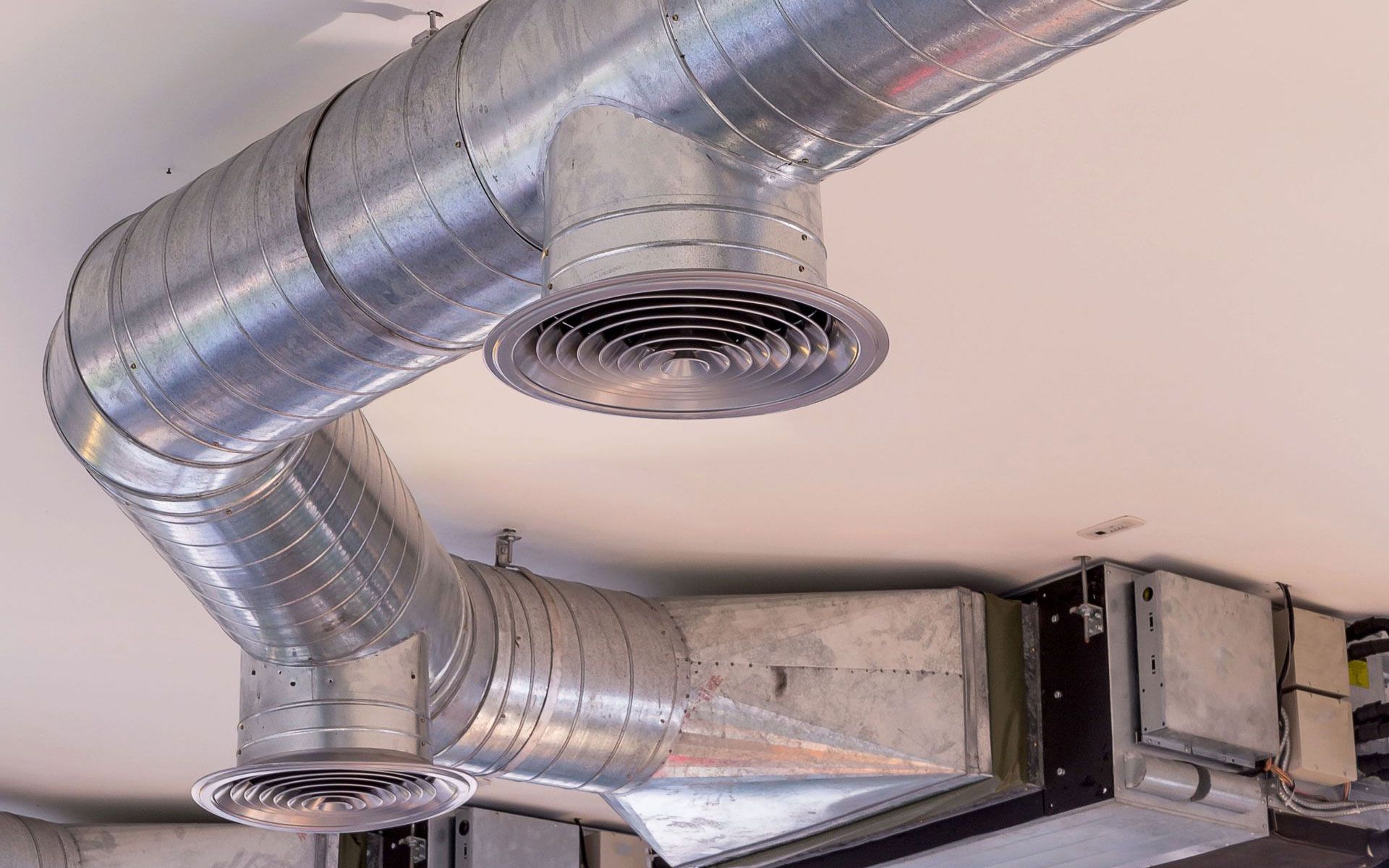 Silver metallic HVAC ductwork with round air diffusers mounted to a ceiling.