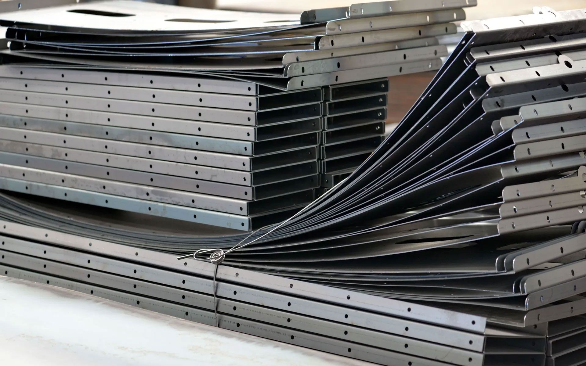 Stacks of dark gray, perforated metal shelving components arranged in a warehouse setting.