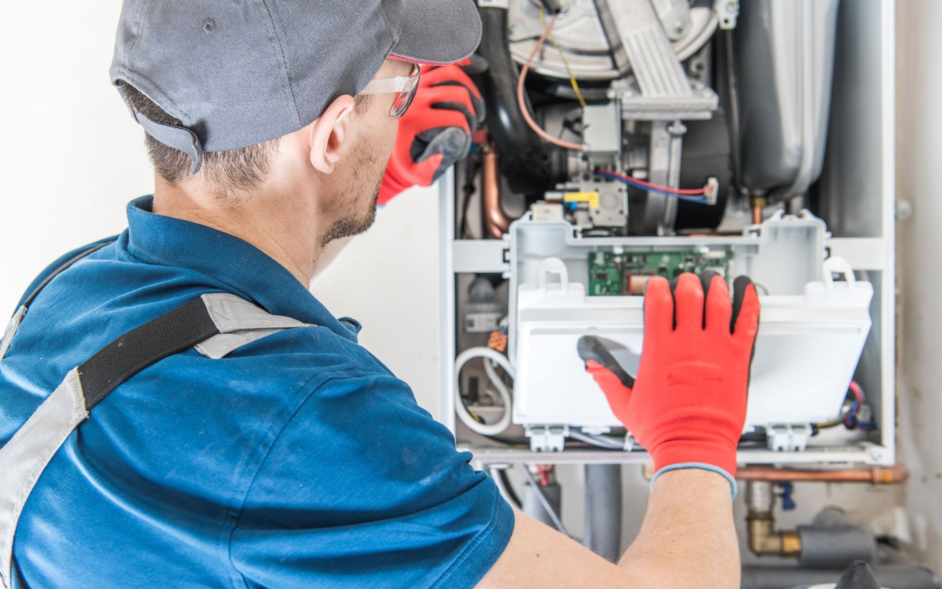 A technician in a blue uniform and red gloves repairs a wall-mounted gas boiler, focusing on its internal components.