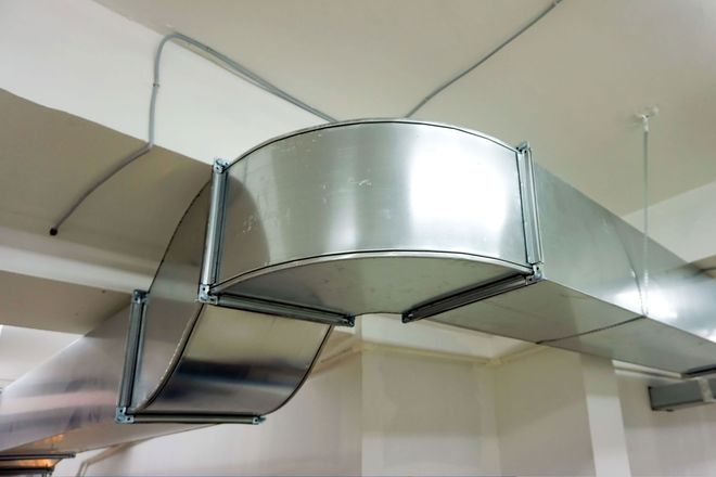 A metallic, rectangular HVAC duct system with a curved elbow joint suspended from a white ceiling.