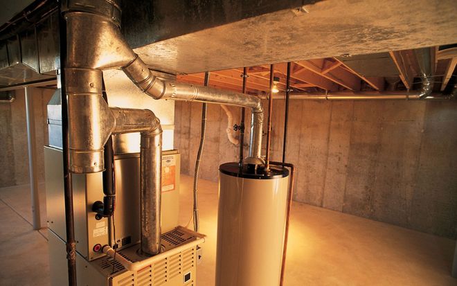A furnace and a water heater stand in a residential basement with concrete walls and exposed ceiling joists.