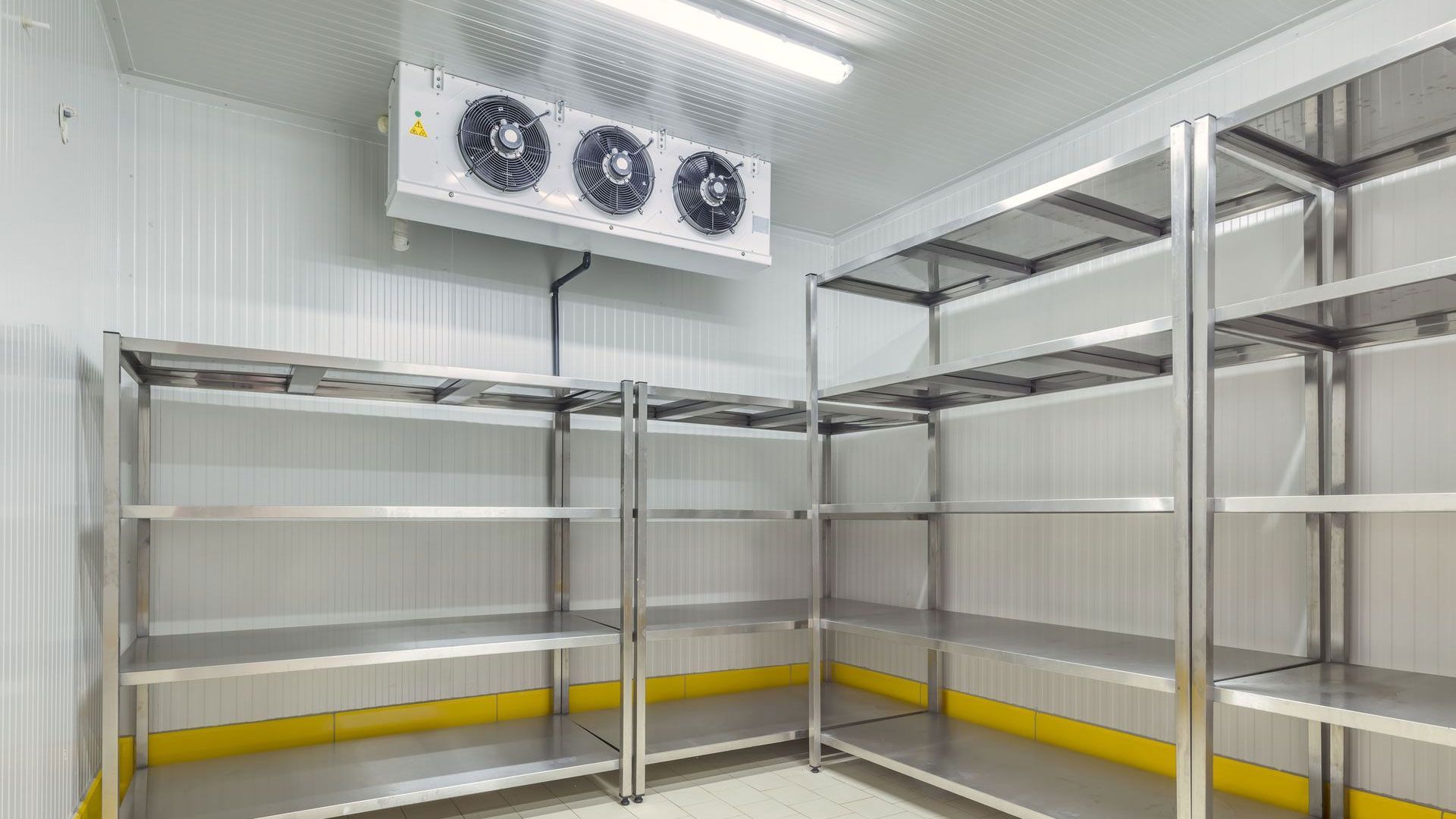 An empty walk-in cooler featuring stainless steel shelving units and a ceiling-mounted refrigeration unit.