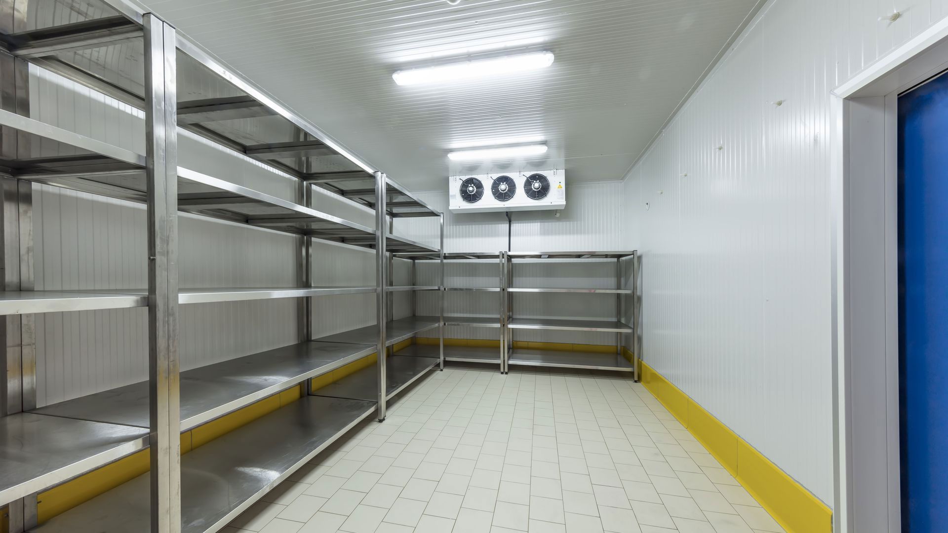 An empty walk-in cooler or industrial freezer with stainless steel shelving, white walls, and a blue door.