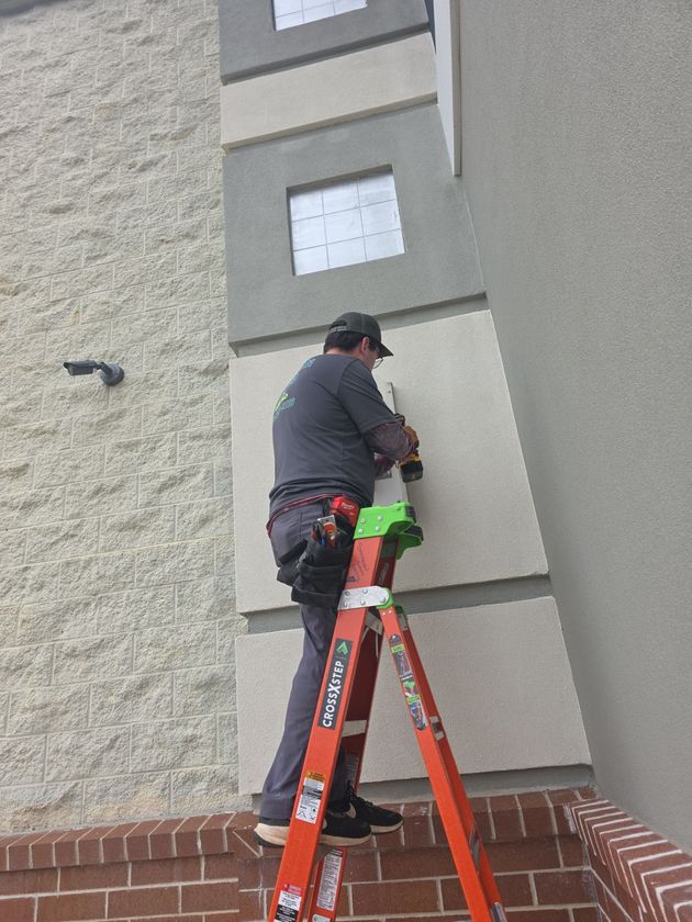 Person on ladder using a drill on building exterior; cream and grey color scheme.