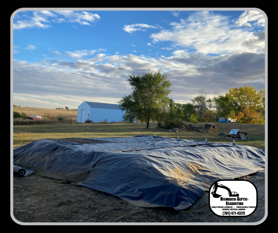A large tarp is sitting in a field with a barn in the background.