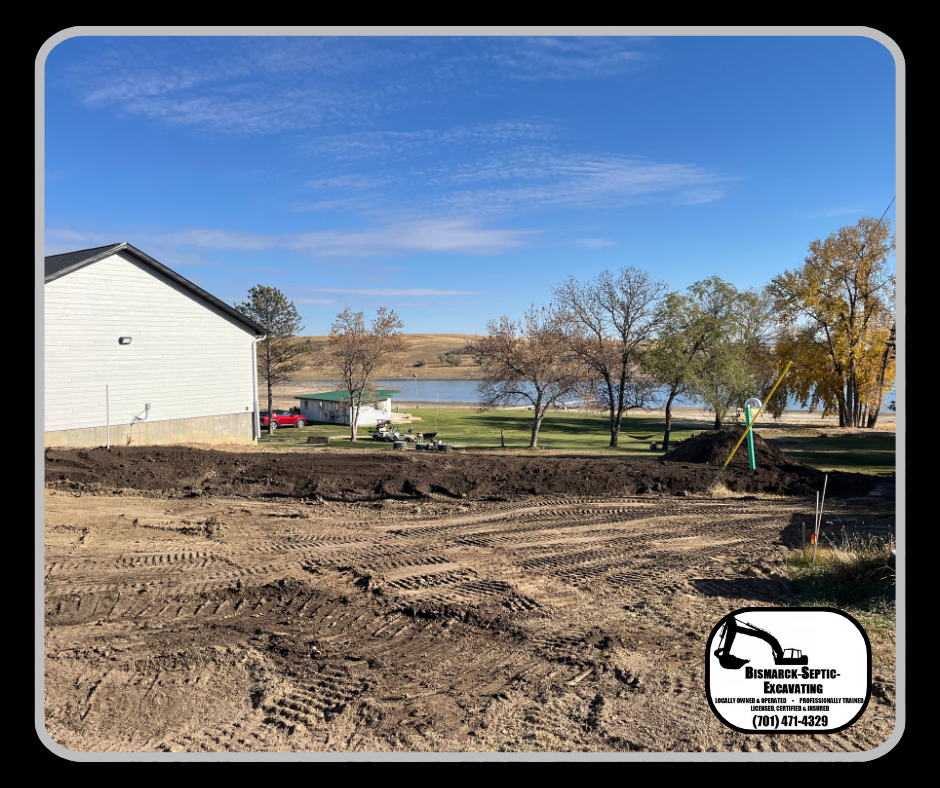 A large dirt field with a house in the background and a lake in the background.