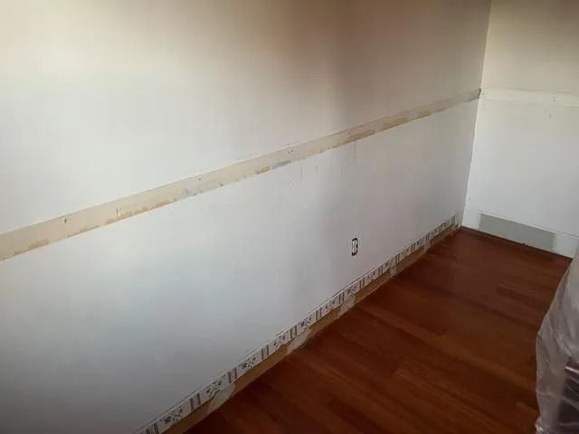 Empty room with white walls, wood floor, and a strip of unfinished paint along the wall