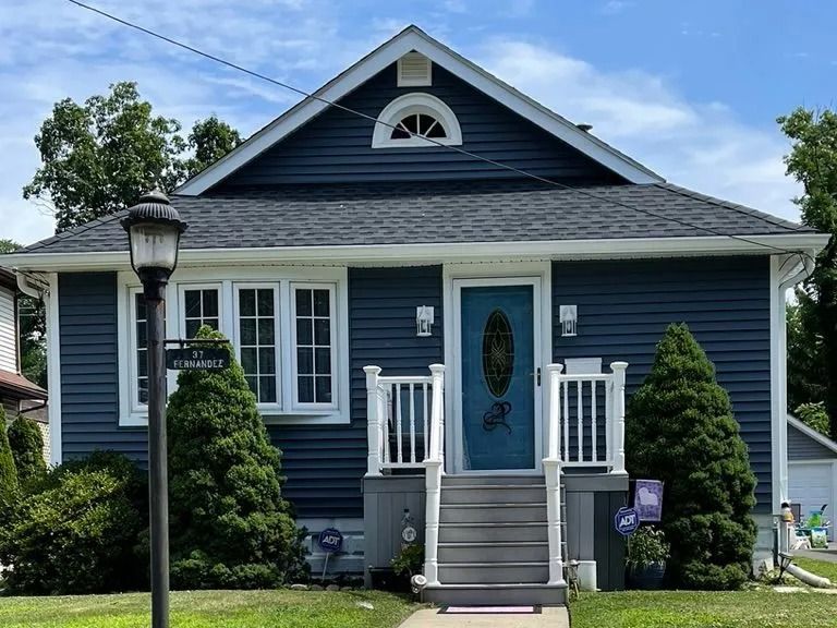 Blue cottage with white trim, front steps, and a small porch under a gray roof on a sunny day