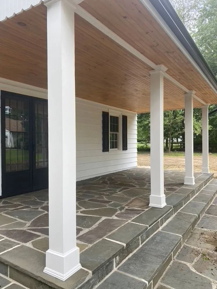 White house porch with square columns, stone flooring, and a black front door.