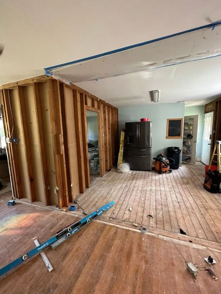 Partially gutted room with exposed wall studs, tools on the floor, and a black cabinet against the far wall
