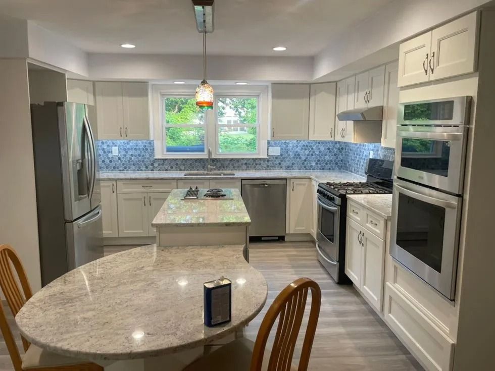 Bright modern kitchen with white cabinets, stainless appliances, blue tile backsplash, and a round table in foreground