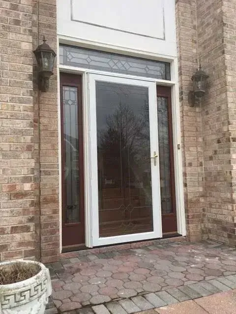 Front entrance with glass door and sidelights in a brick facade, framed by stone and paver walkway.