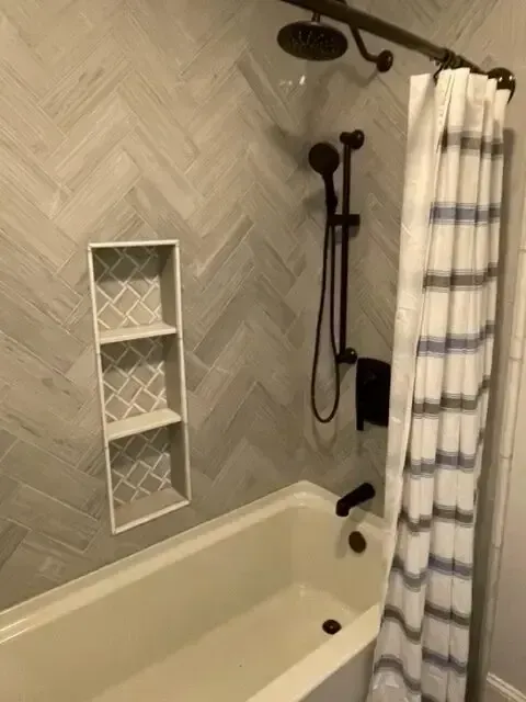 Modern bathroom with herringbone-tile walls, white tub, shower curtain, and recessed wall shelf.