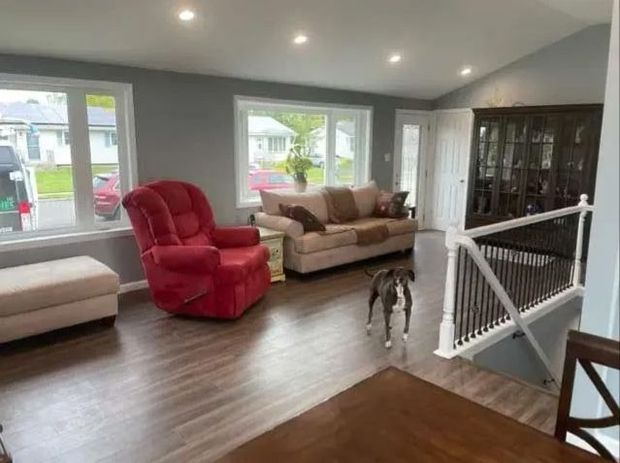 Bright living room with red recliner, beige sofa, hardwood floors, and a staircase railing