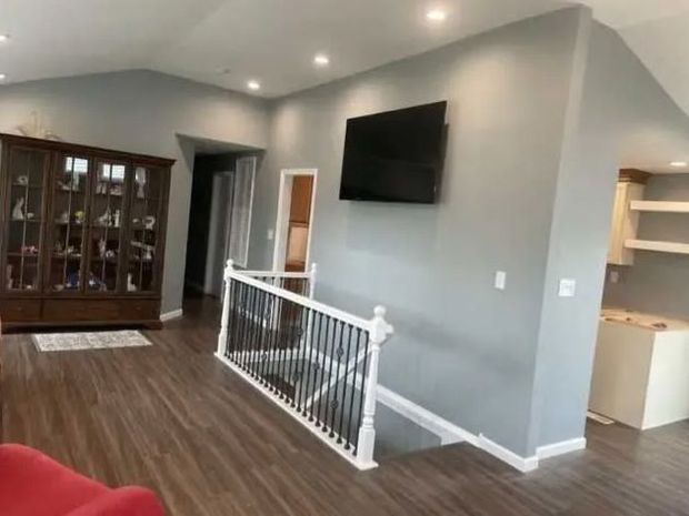 Bright living room with gray walls, hardwood floors, wall-mounted TV, and stair railing.