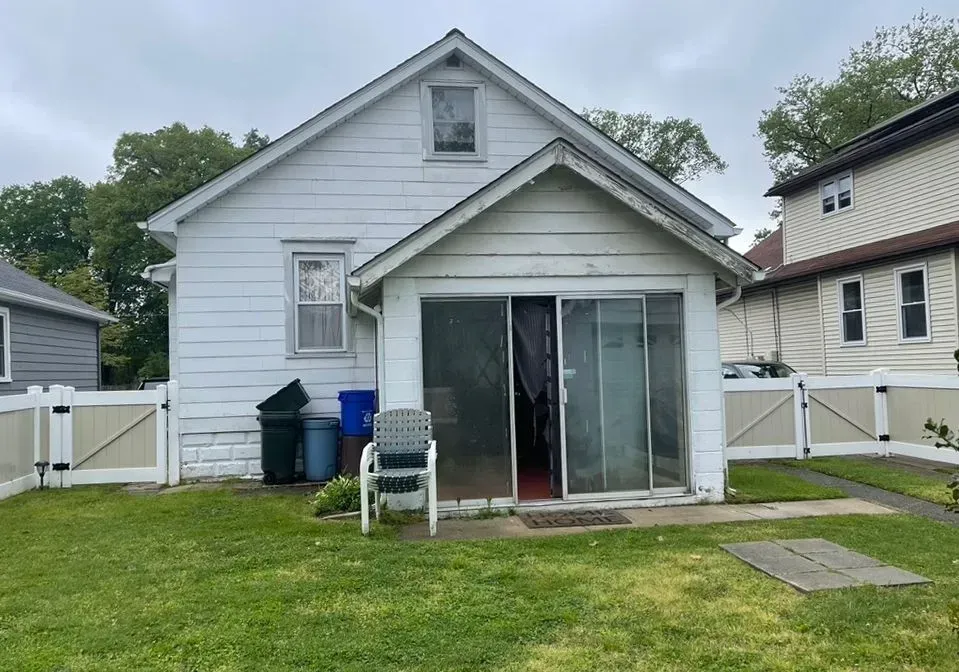 White house with a sliding glass door, small porch, lawn, and fenced backyard under cloudy skies