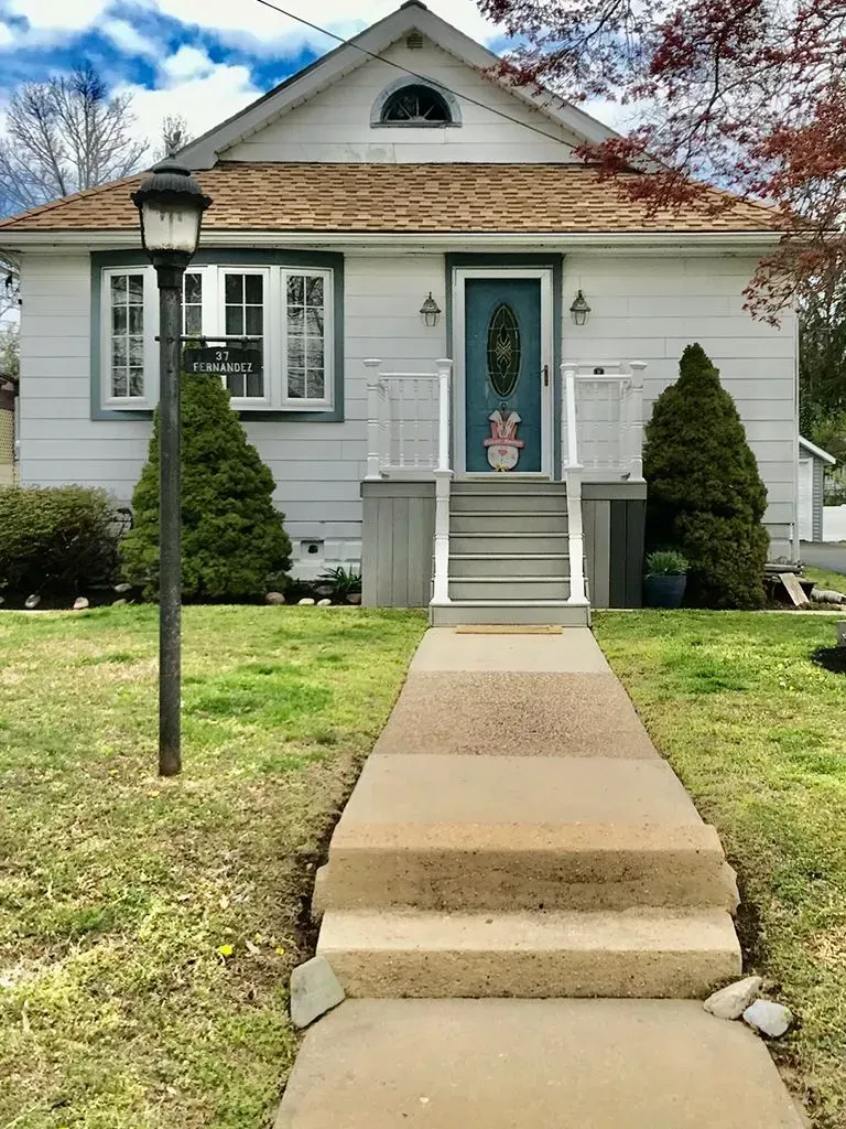 Small white house with a blue front door, front steps, walkway, and lawn under a partly cloudy sky
