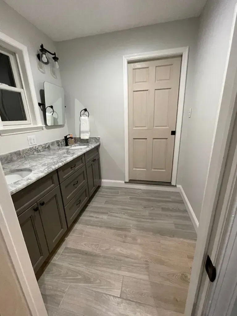 Narrow bathroom with gray vanity, marble countertop, mirror, and closed beige door