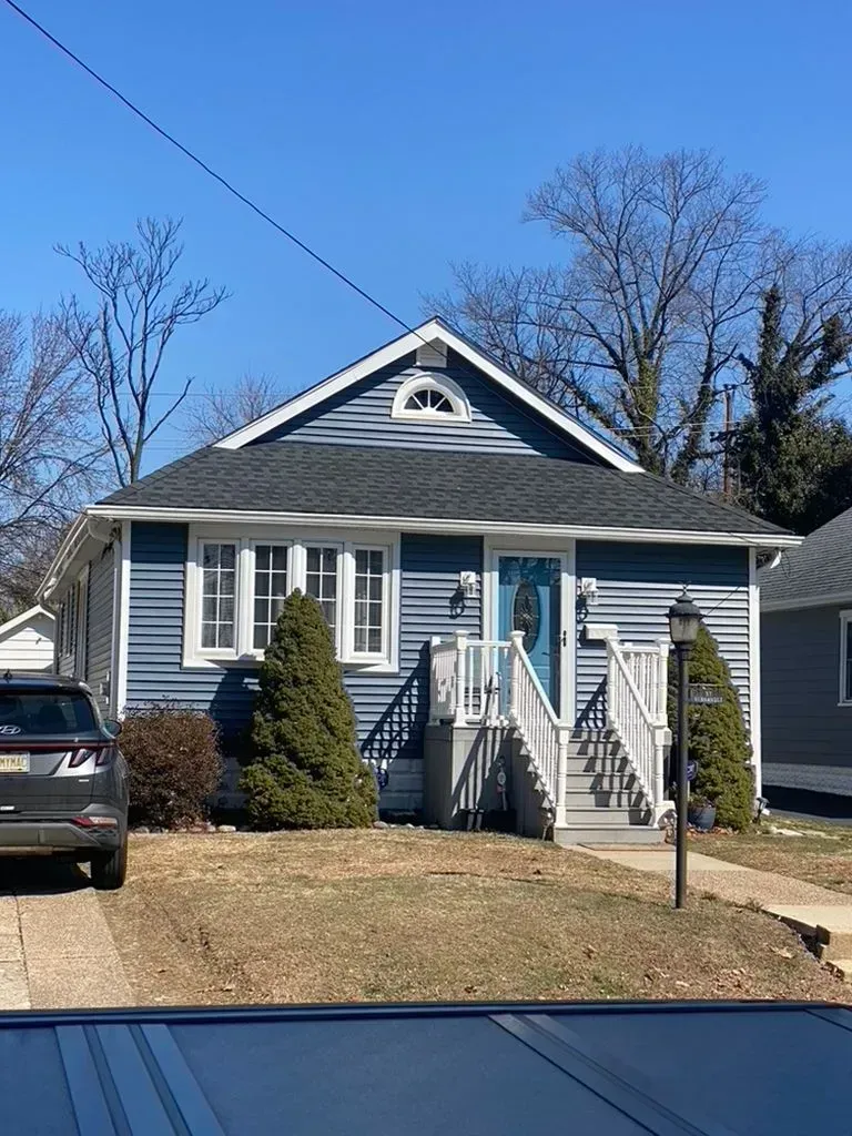Small gray house with white trim, front steps, and a driveway under a clear blue sky.