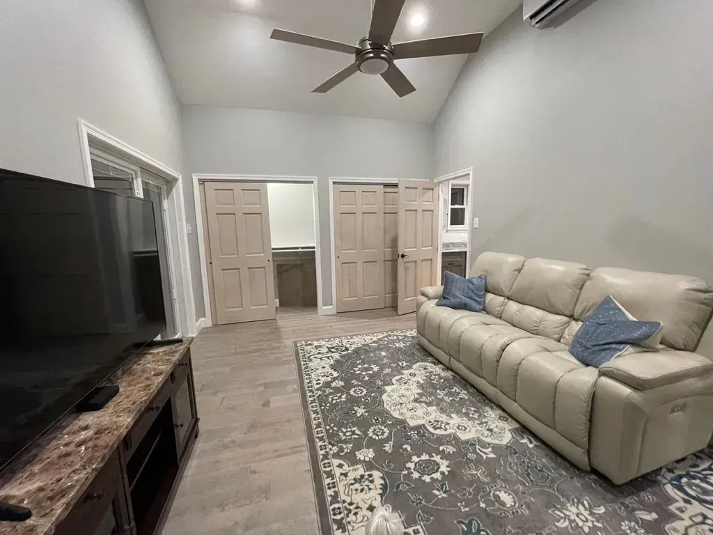 Living room with beige sofa, patterned rug, TV stand, ceiling fan, and double closet doors