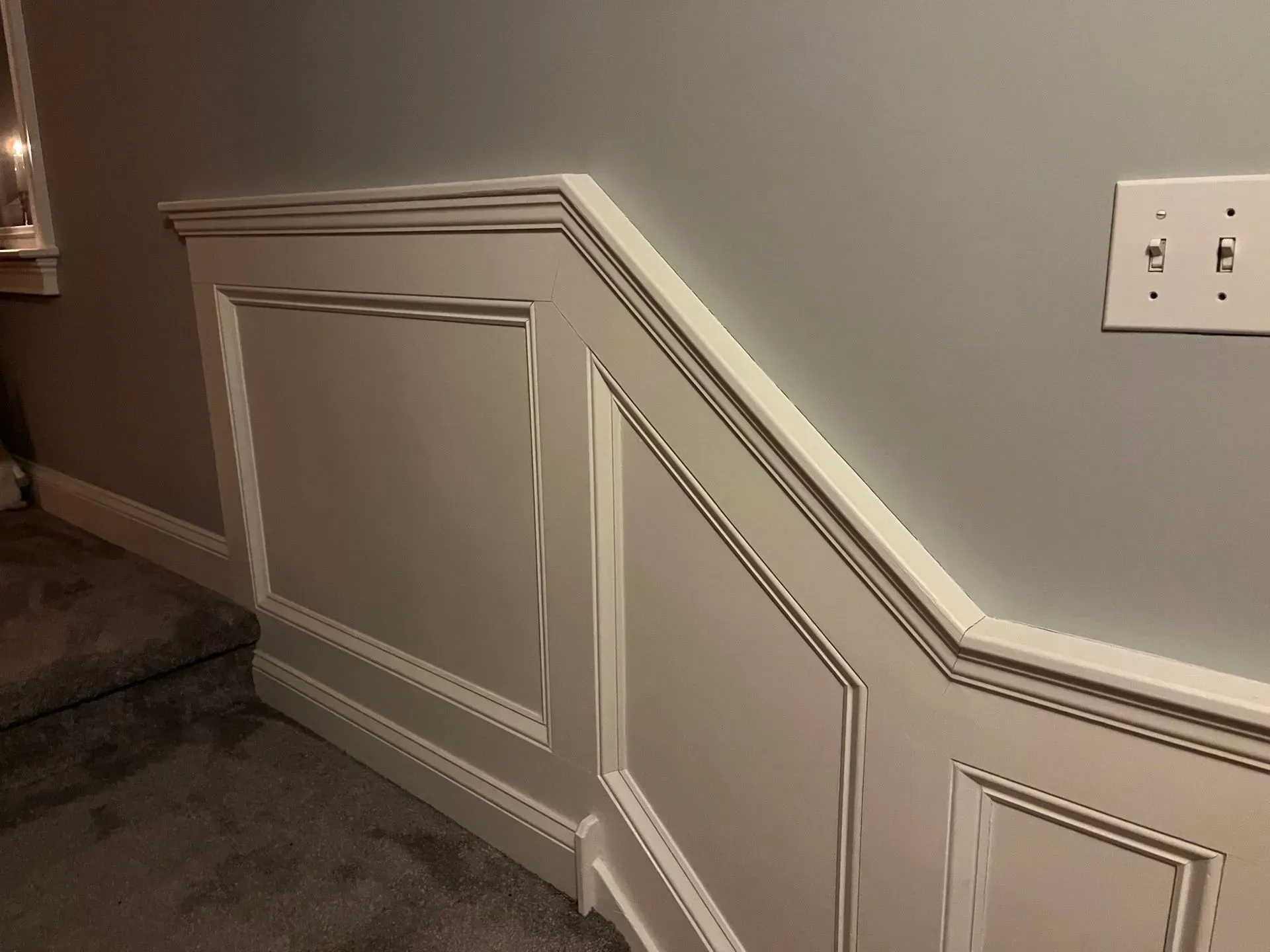 White paneled wainscoting with trim on a gray hallway wall and carpeted floor