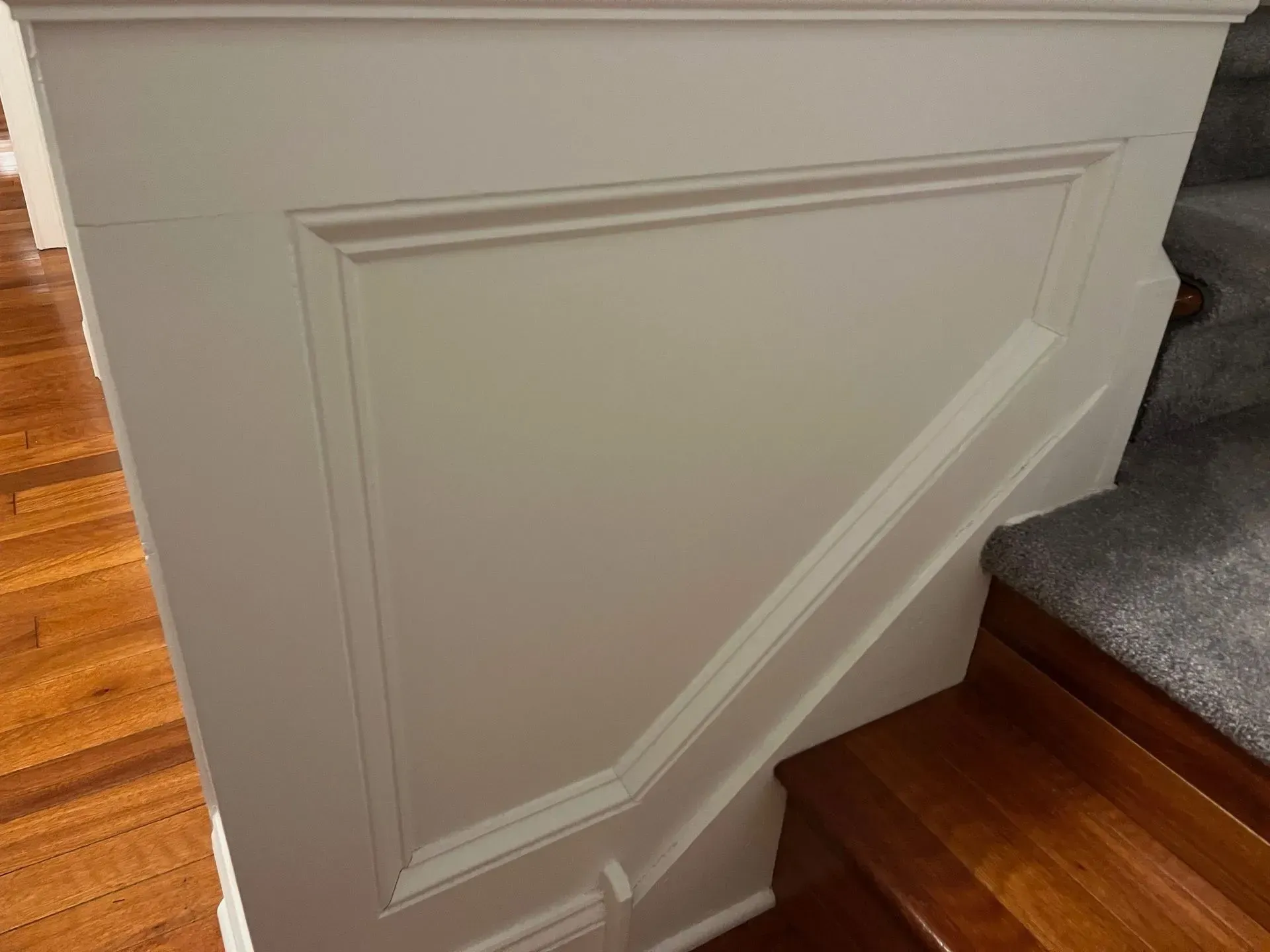 White paneled stairway half wall beside carpeted steps and hardwood floor