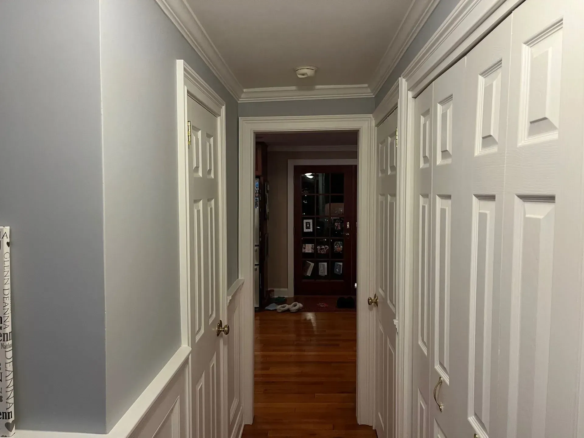 A narrow gray hallway with white doors and wood floors, leading to a room at the end.