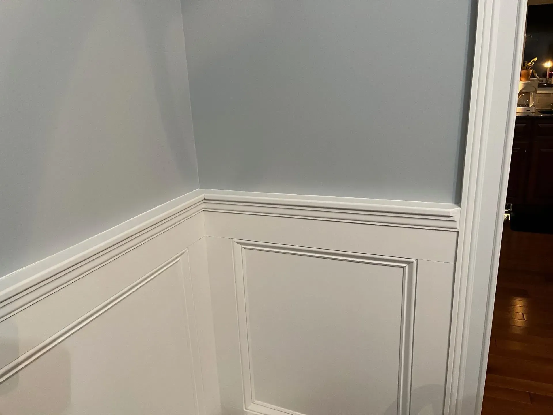 White paneled wainscoting and gray walls in a corner hallway with hardwood floor