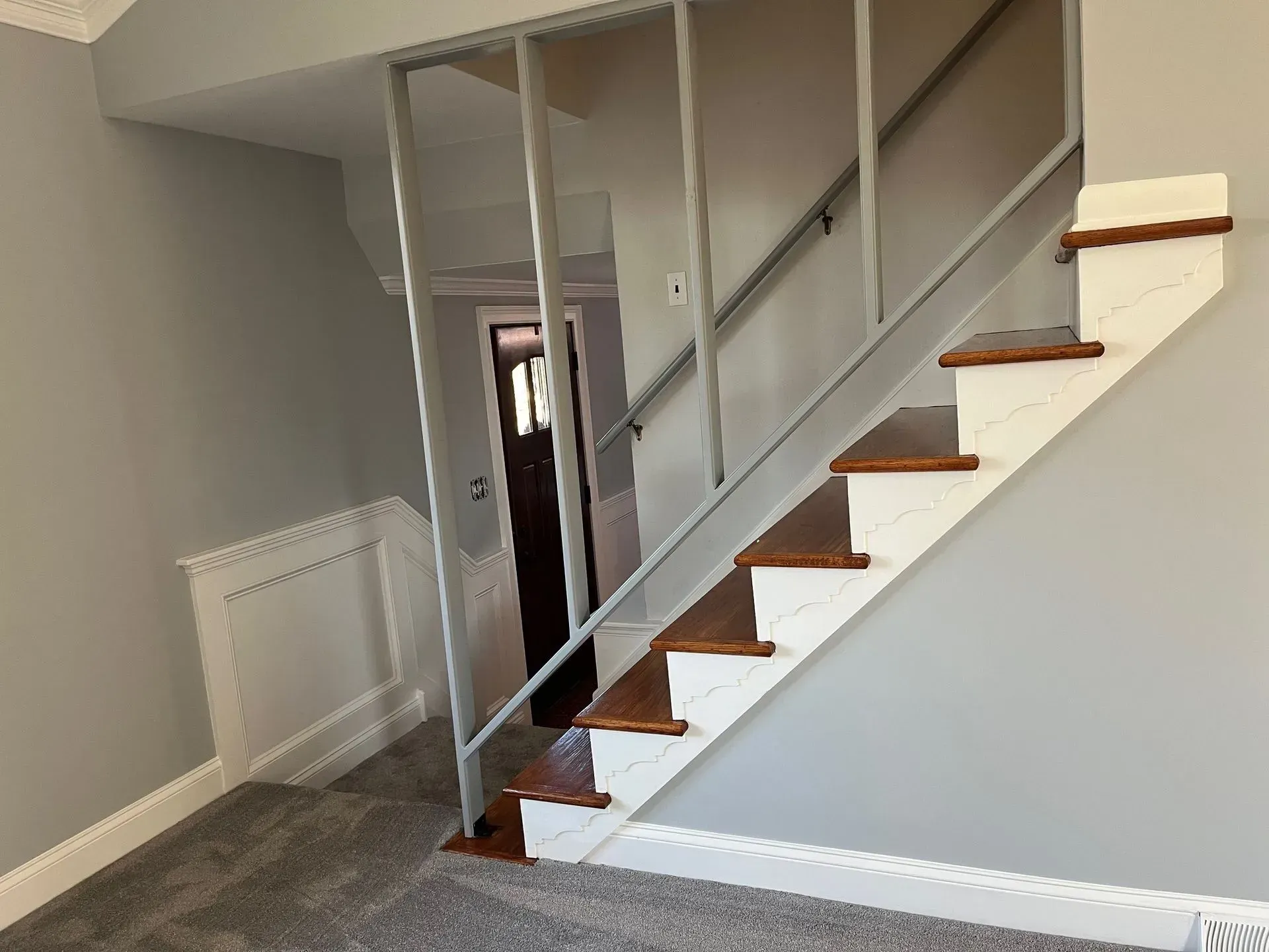 Interior staircase with wooden treads, white railing, and gray carpeted floor in a home hallway