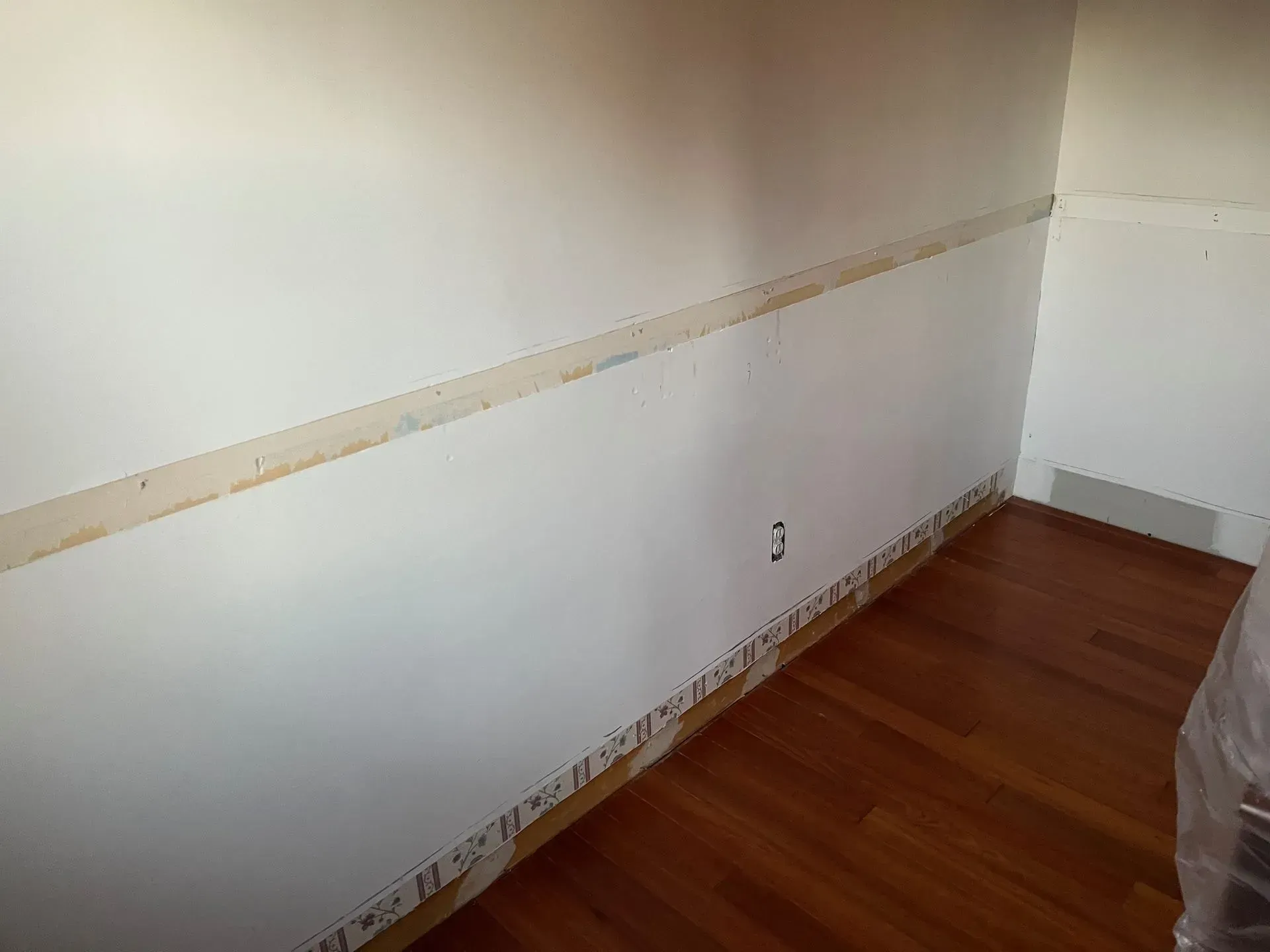 Empty room with white walls, wood floor, and a chair rail trim near the corner.