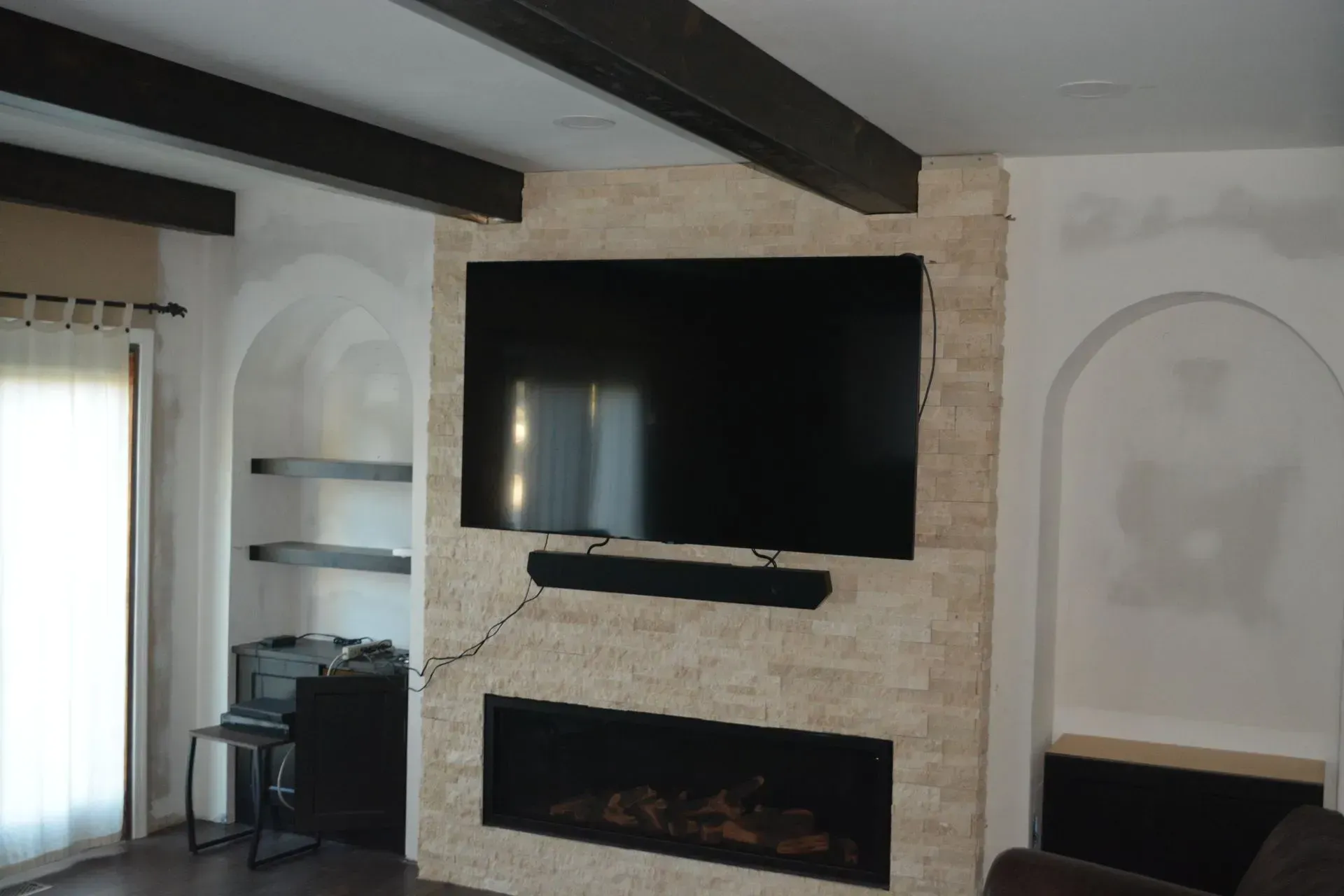 Modern living room with wall-mounted TV above a stone fireplace and dark ceiling beams