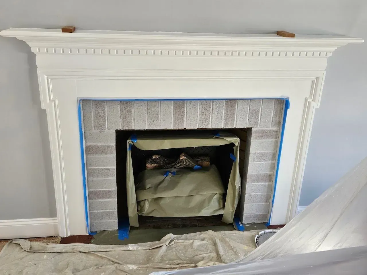 White fireplace mantel with blue painter’s tape around the opening during renovation work