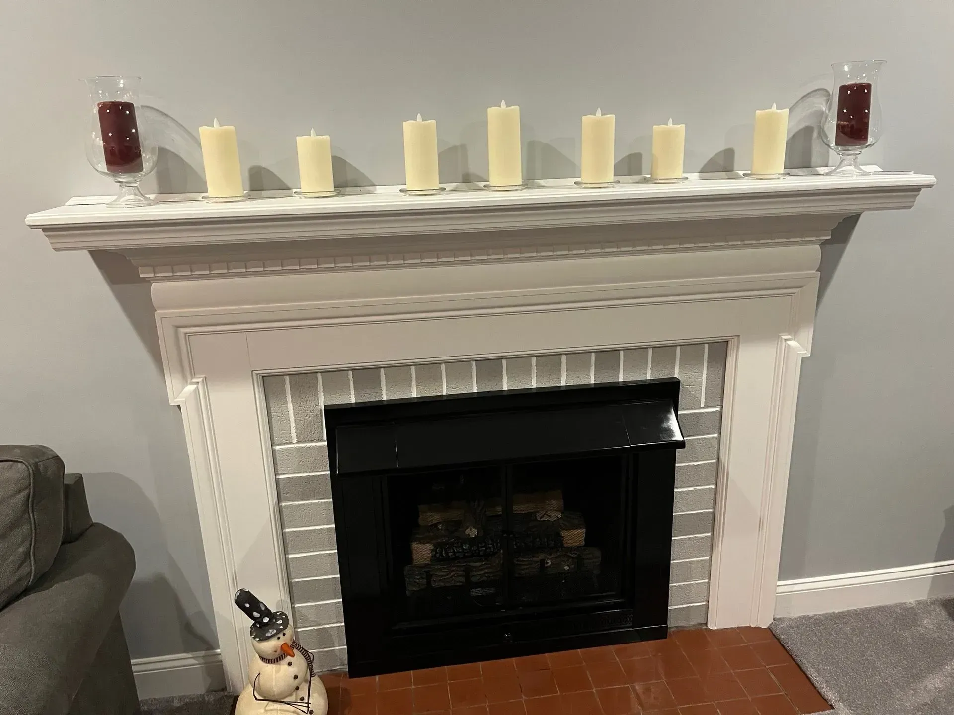 White fireplace mantel with candles, framed by light gray walls and a small holiday decoration at the base