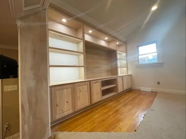Built-in shelving and cabinets along a sloped-wall room with hardwood floor and small window