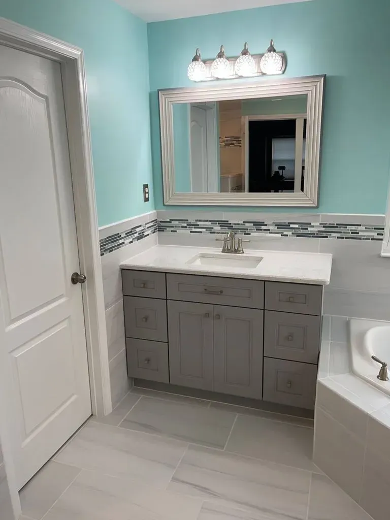 Bright bathroom vanity with gray cabinets, white countertop, turquoise walls, and a large mirror.