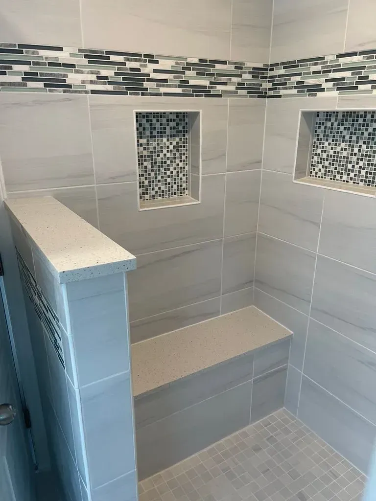 Empty tiled shower with built-in bench, mosaic accent border, and two recessed wall niches.