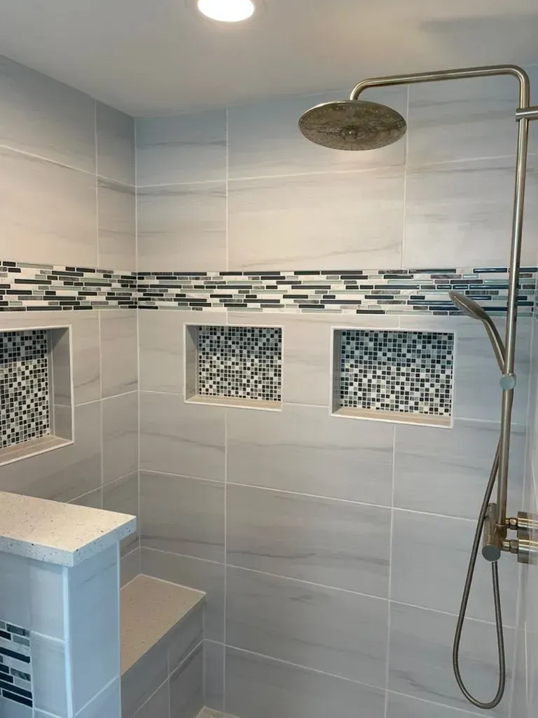 Modern tiled shower with mosaic accents, built-in shelves, and a chrome rainfall showerhead.