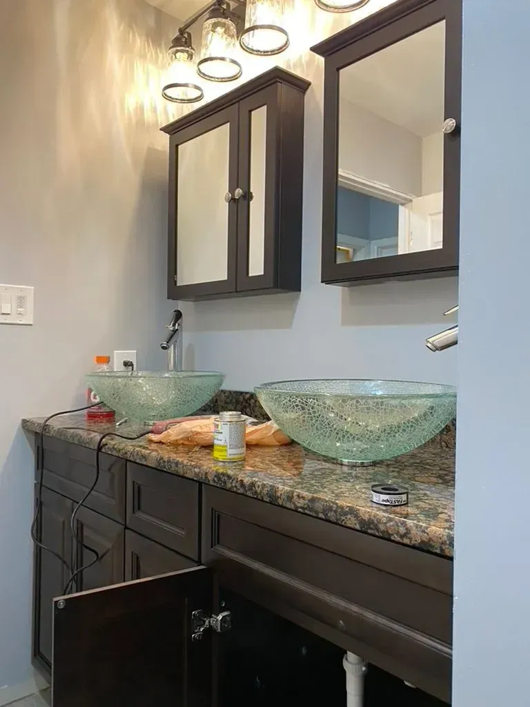 Modern bathroom vanity with two vessel sinks, granite countertop, and mirrored cabinets