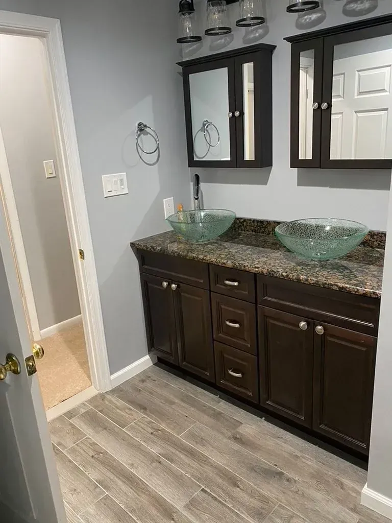 Bathroom vanity with dark cabinets, granite countertop, glass vessel sinks, and two mirrors.
