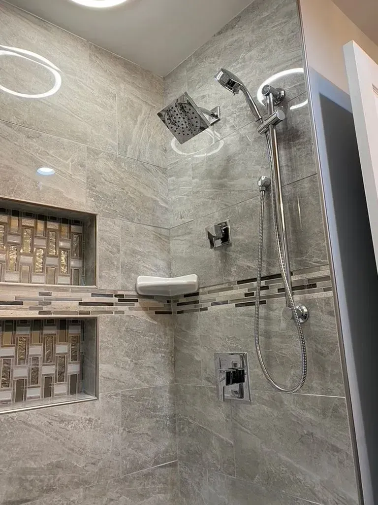 Modern tiled shower with handheld showerhead, built-in niches, and a corner shelf in a bathroom.