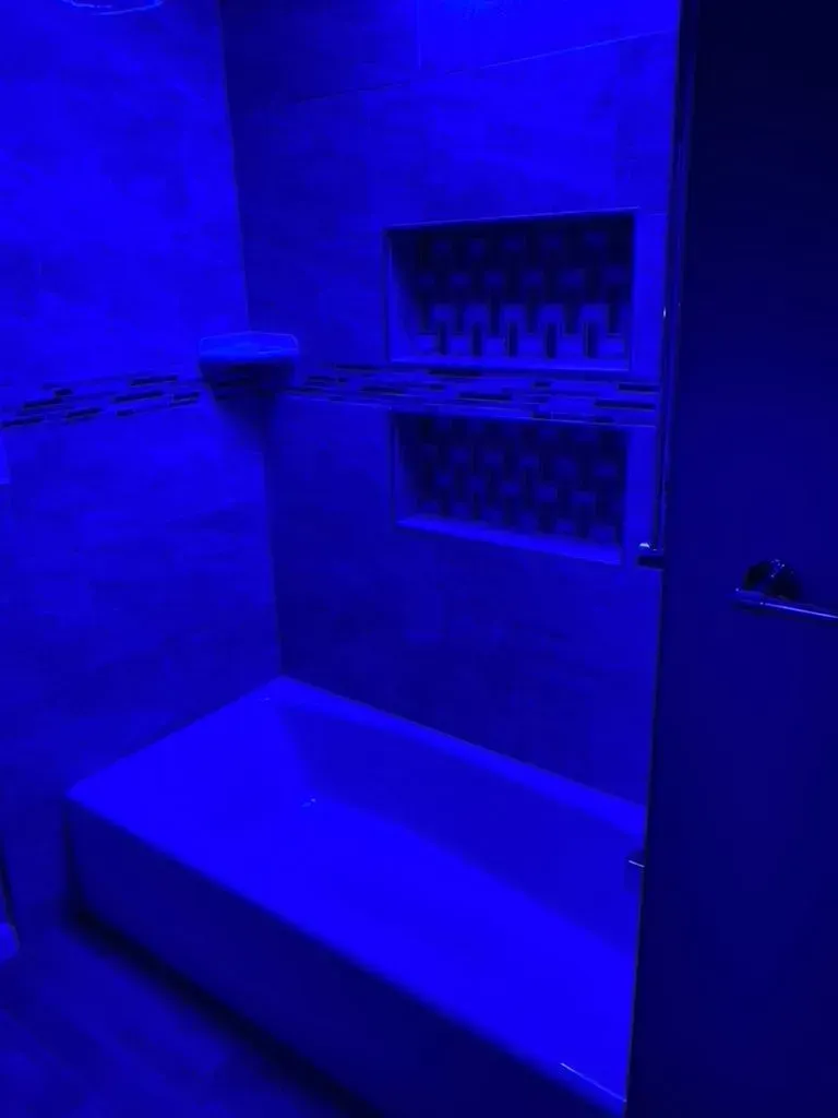 Blue-lit bathroom with a bathtub and wall-mounted shelf above it