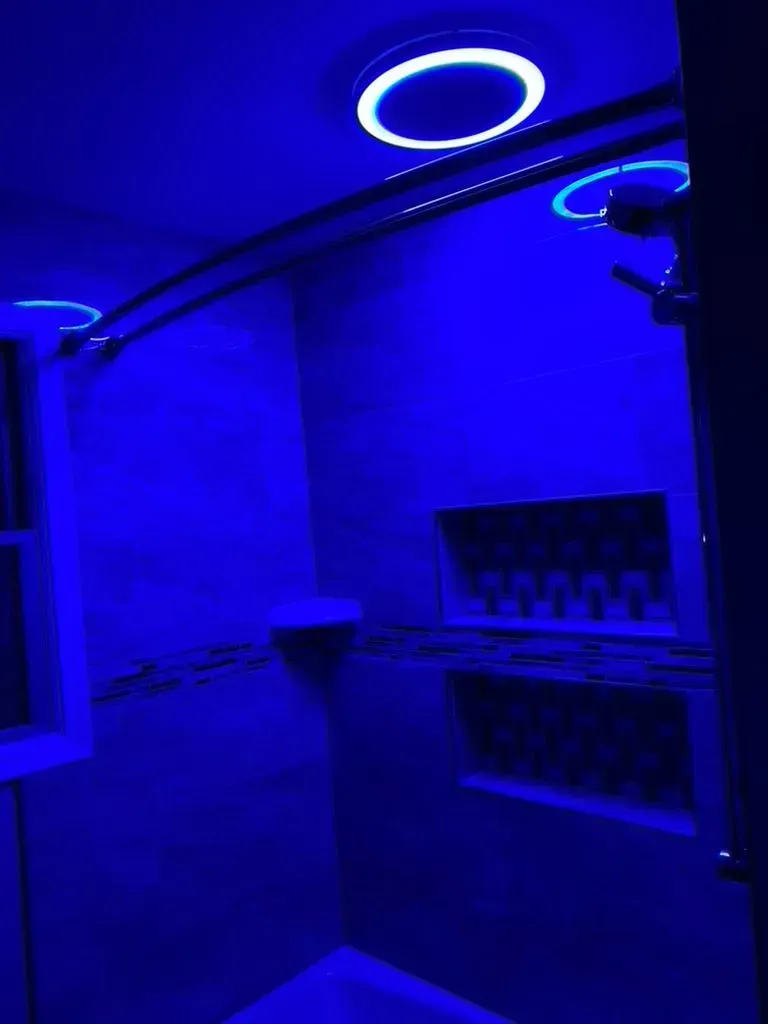 Blue-lit modern bathroom with shower, sink, and circular ceiling light