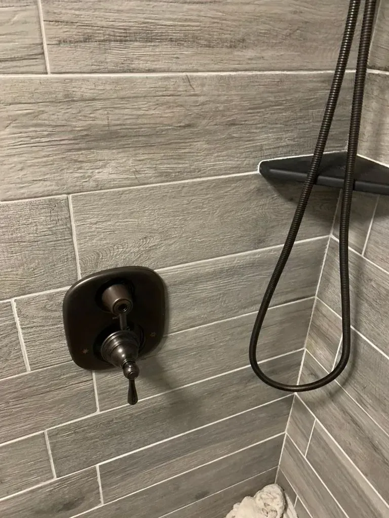Shower wall with chrome control valve, black showerhead, and gray tile surround.