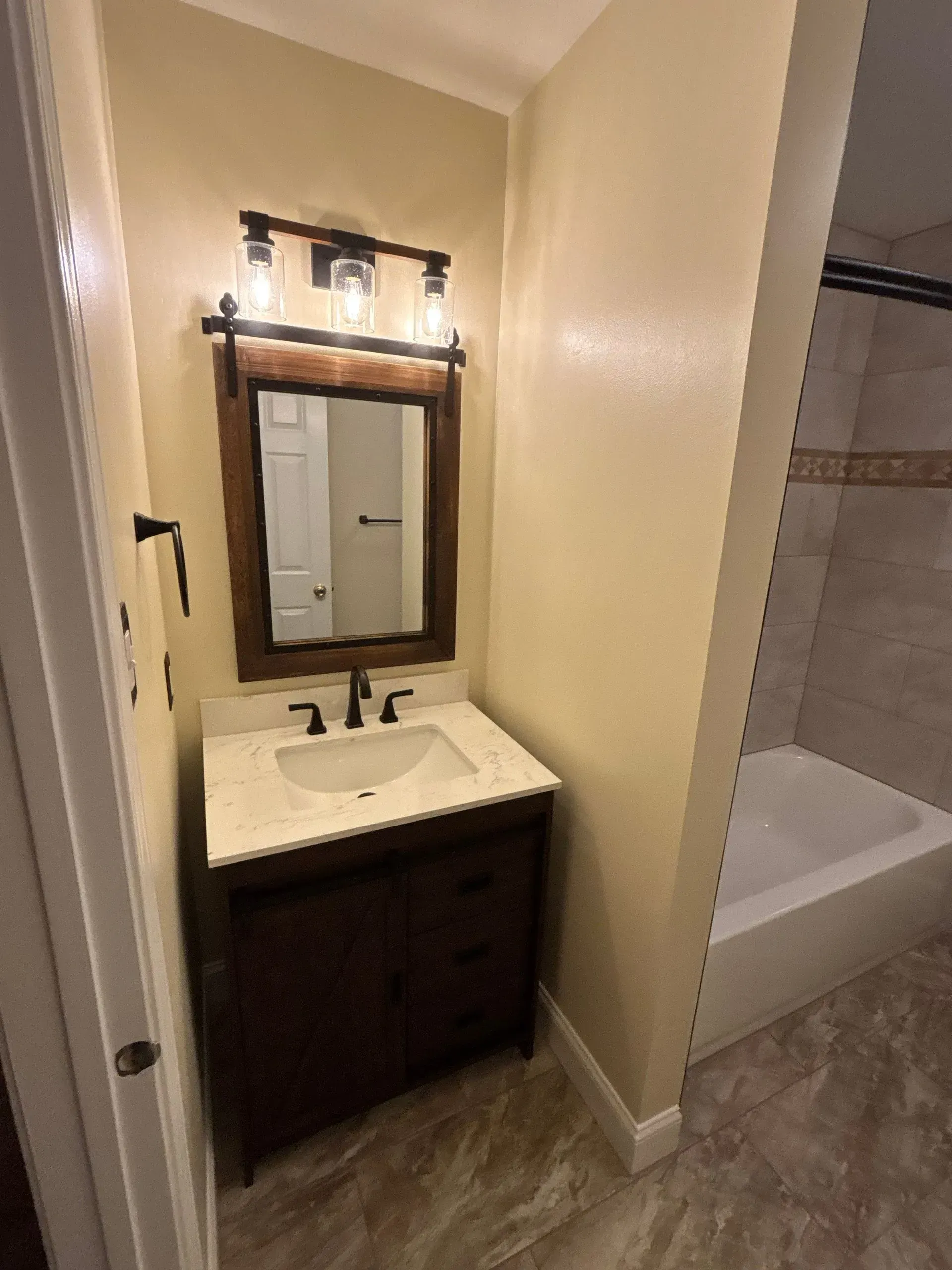 Small bathroom vanity with mirror and light, beside a partially visible bathtub.