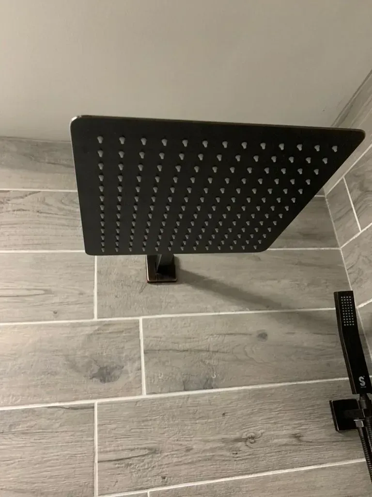 Black square rainfall shower head on a wall-mounted arm over gray tile flooring.