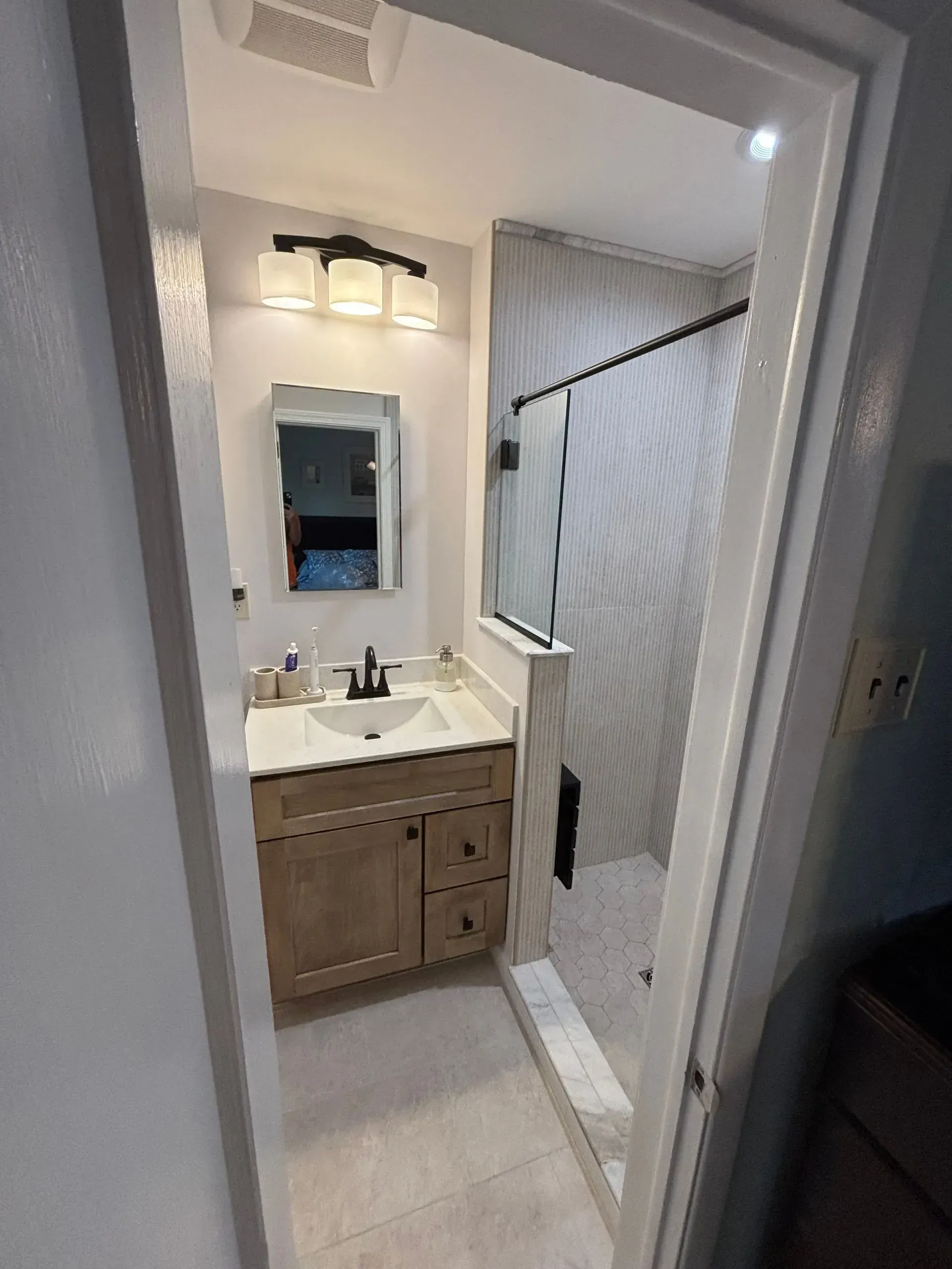 Small bathroom vanity with mirror, light fixture, and white chevron shower curtain in a narrow hallway.