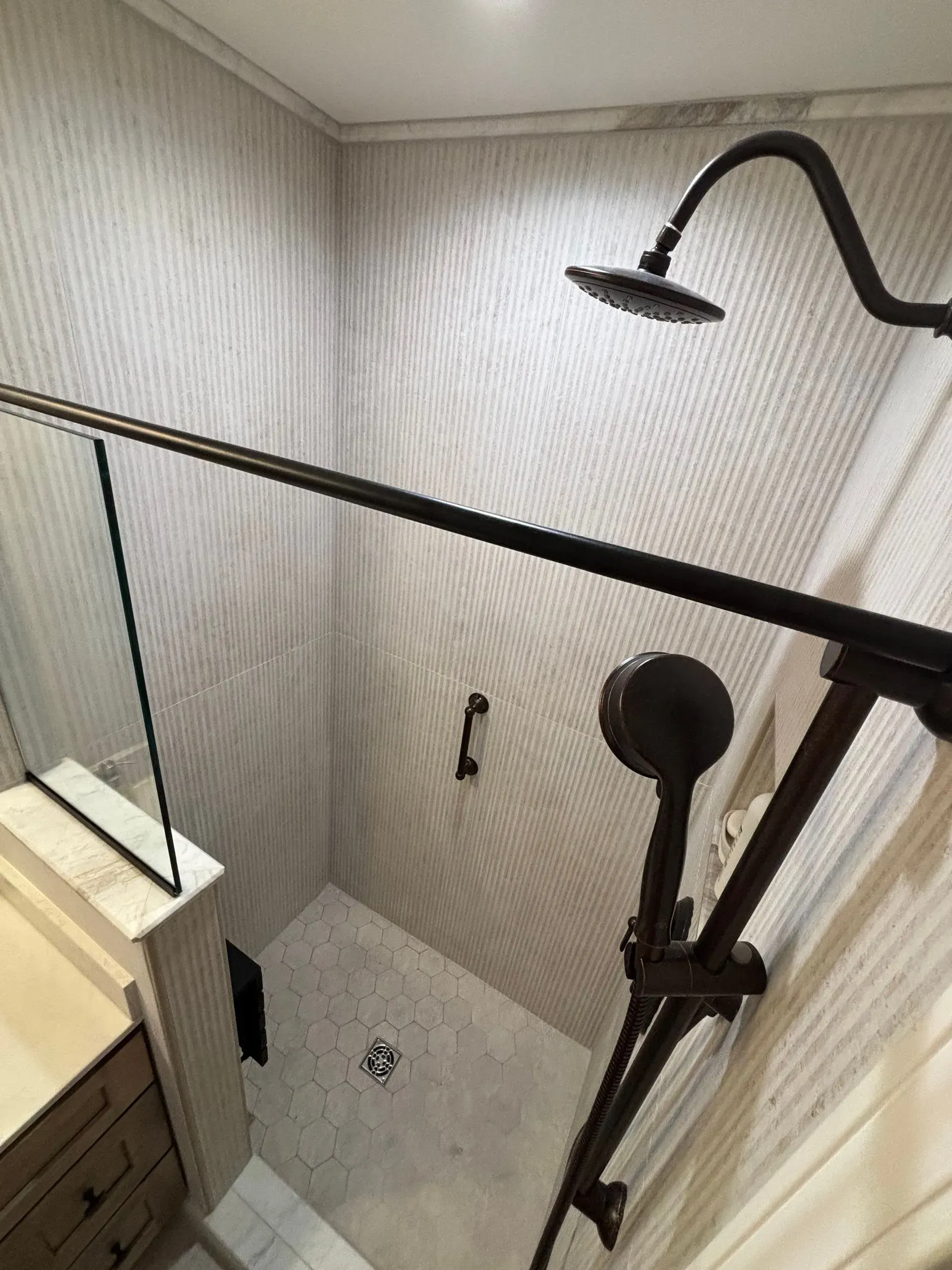 Small tiled shower with black grab bars and a handheld showerhead.