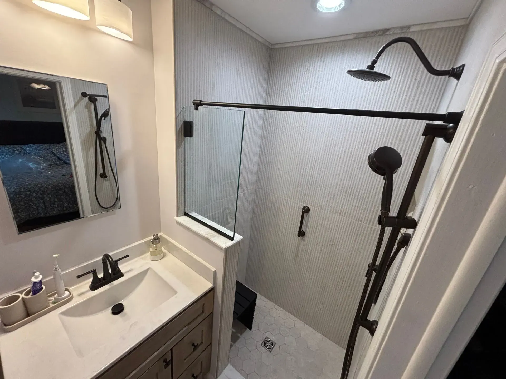 Small bathroom with walk-in shower, glass door, black shower rail, and white vanity sink.
